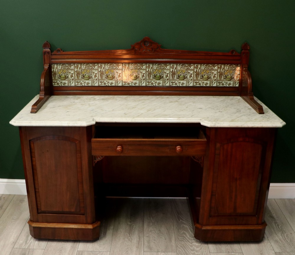 A Victorian Aesthetic Movement mahogany washstand featuring a white marble top, a tiled gallery splashback with floral motifs, two pedestal cupboards, and a central drawer. View III