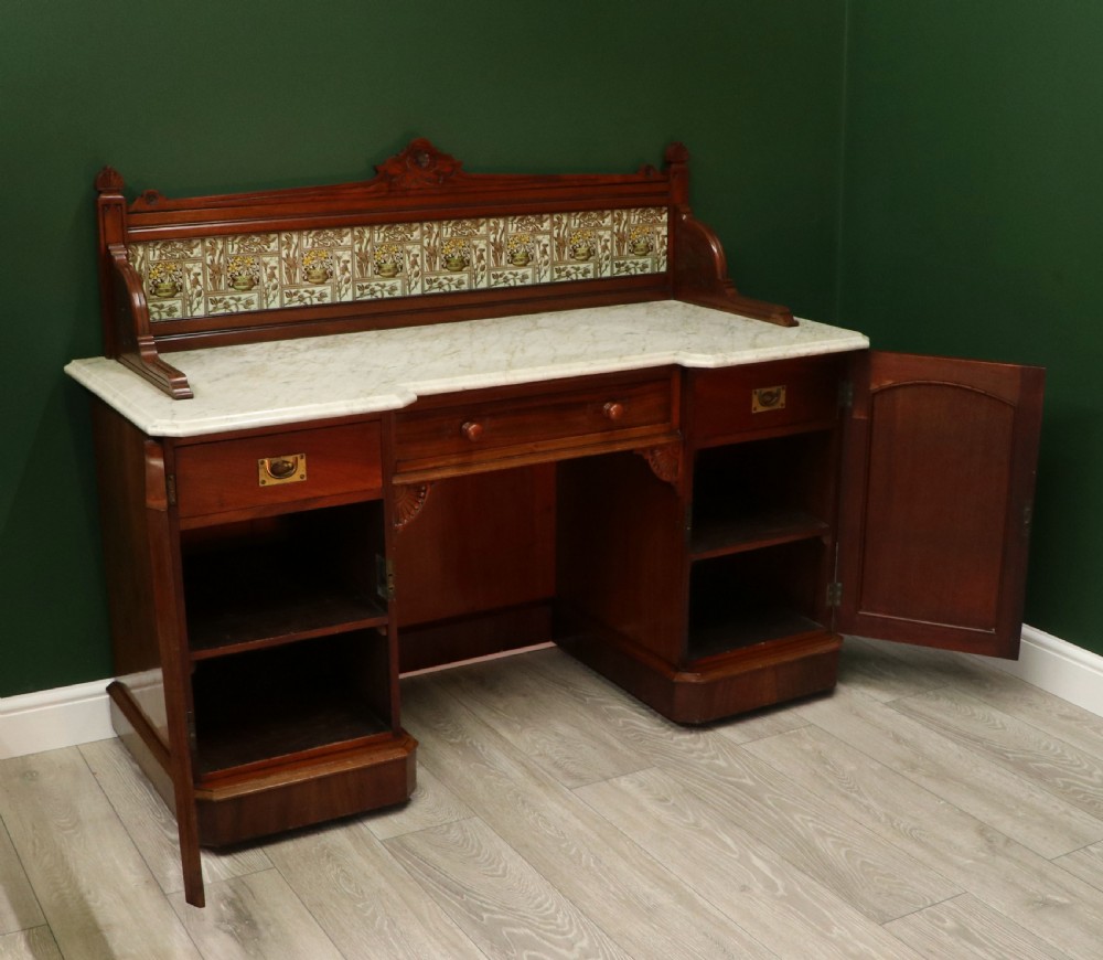 A Victorian Aesthetic Movement mahogany washstand featuring a white marble top, a tiled gallery splashback with floral motifs, two pedestal cupboards, and a central drawer. View VII