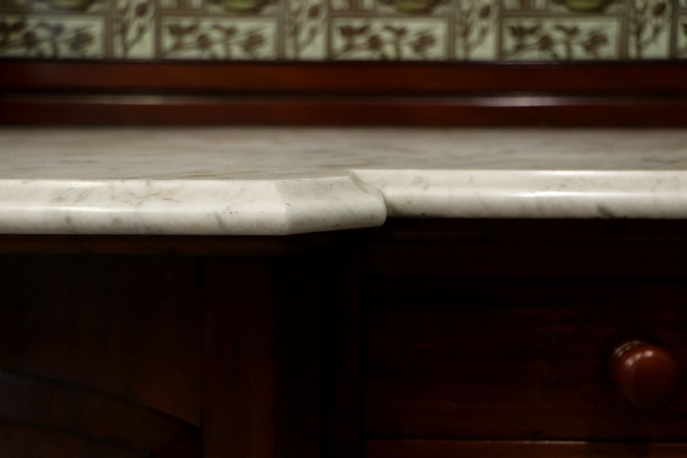 A Victorian Aesthetic Movement mahogany washstand featuring a white marble top, a tiled gallery splashback with floral motifs, two pedestal cupboards, and a central drawer. View XIII
