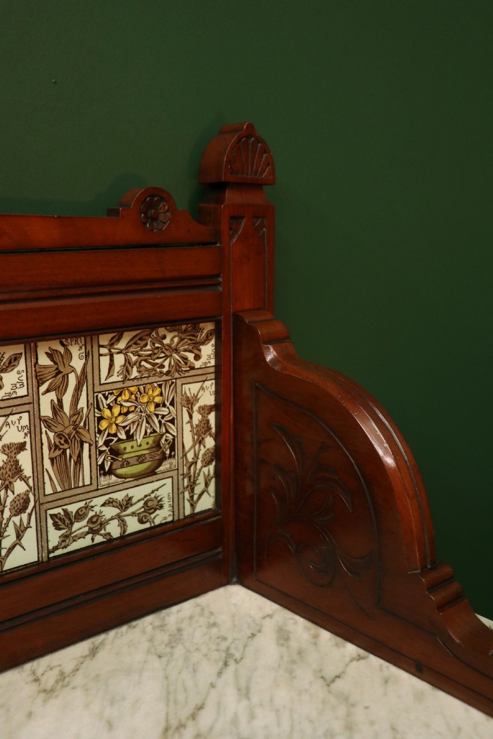 A Victorian Aesthetic Movement mahogany washstand featuring a white marble top, a tiled gallery splashback with floral motifs, two pedestal cupboards, and a central drawer. View XVIII