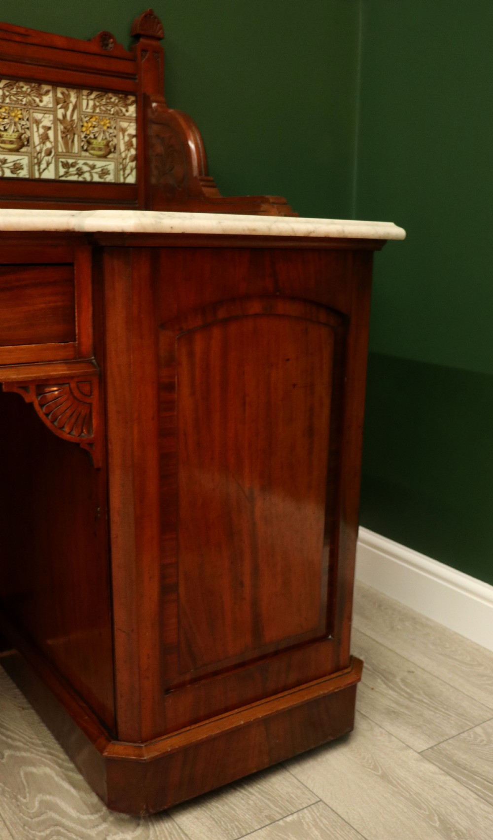 A Victorian Aesthetic Movement mahogany washstand featuring a white marble top, a tiled gallery splashback with floral motifs, two pedestal cupboards, and a central drawer. View XXIII