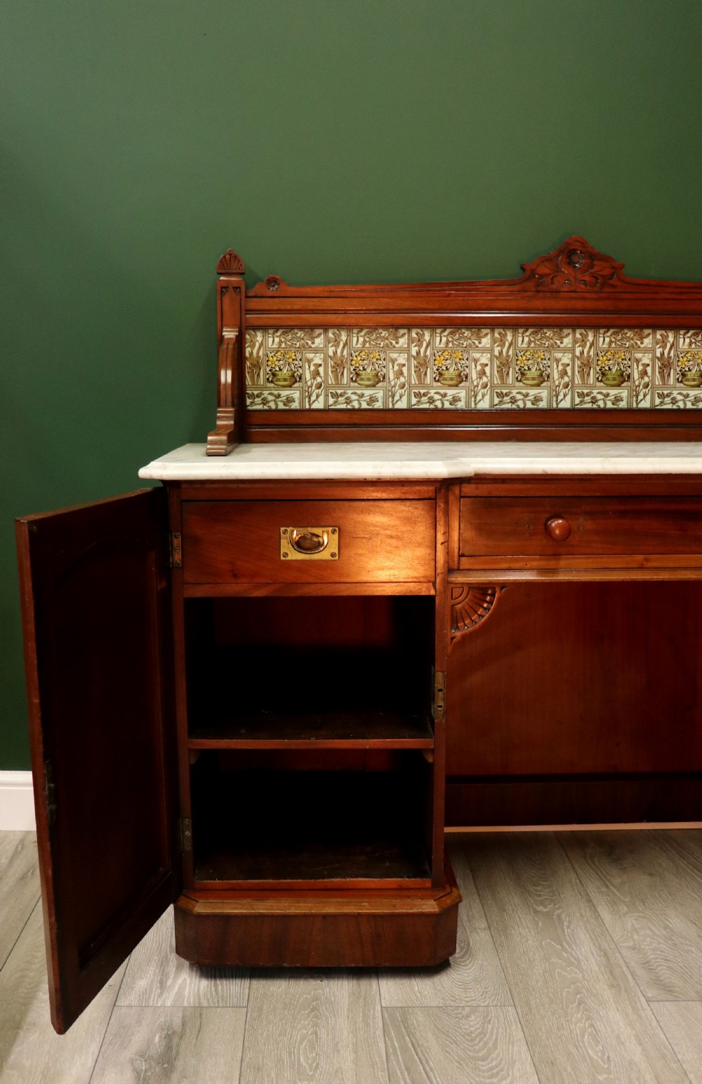 A Victorian Aesthetic Movement mahogany washstand featuring a white marble top, a tiled gallery splashback with floral motifs, two pedestal cupboards, and a central drawer. View XXV
