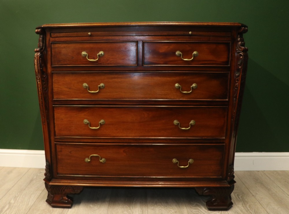 A solid mahogany bachelors chest featuring a pull-out slide, two upper drawers, three lower drawers, brass handles, and carved corner pilasters.