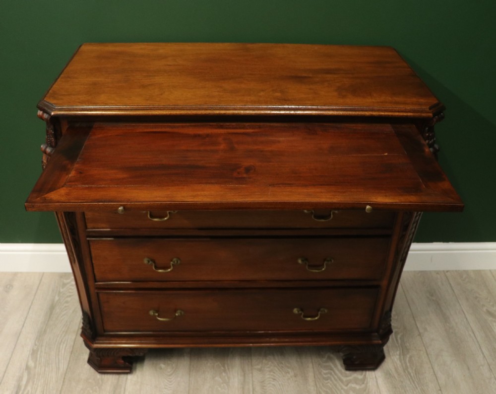 A solid mahogany bachelors chest featuring a pull-out slide, two upper drawers, three lower drawers, brass handles, and carved corner pilasters. View V
