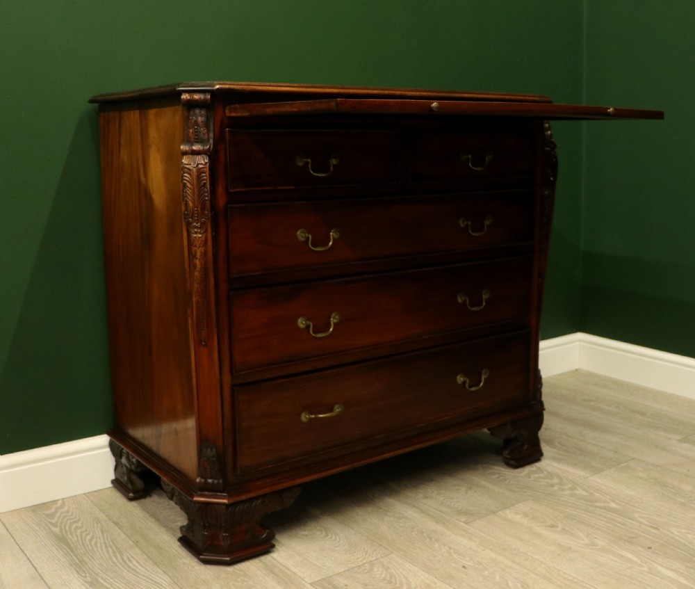 A solid mahogany bachelors chest featuring a pull-out slide, two upper drawers, three lower drawers, brass handles, and carved corner pilasters. View IX