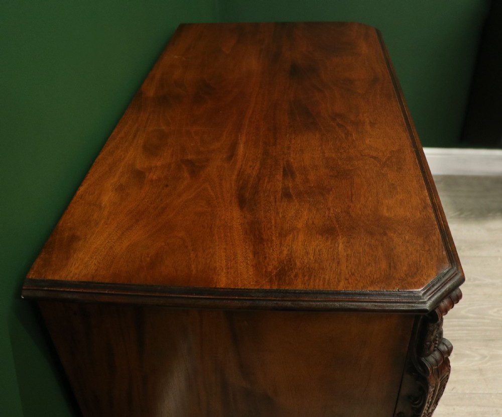 A solid mahogany bachelors chest featuring a pull-out slide, two upper drawers, three lower drawers, brass handles, and carved corner pilasters. View XVI