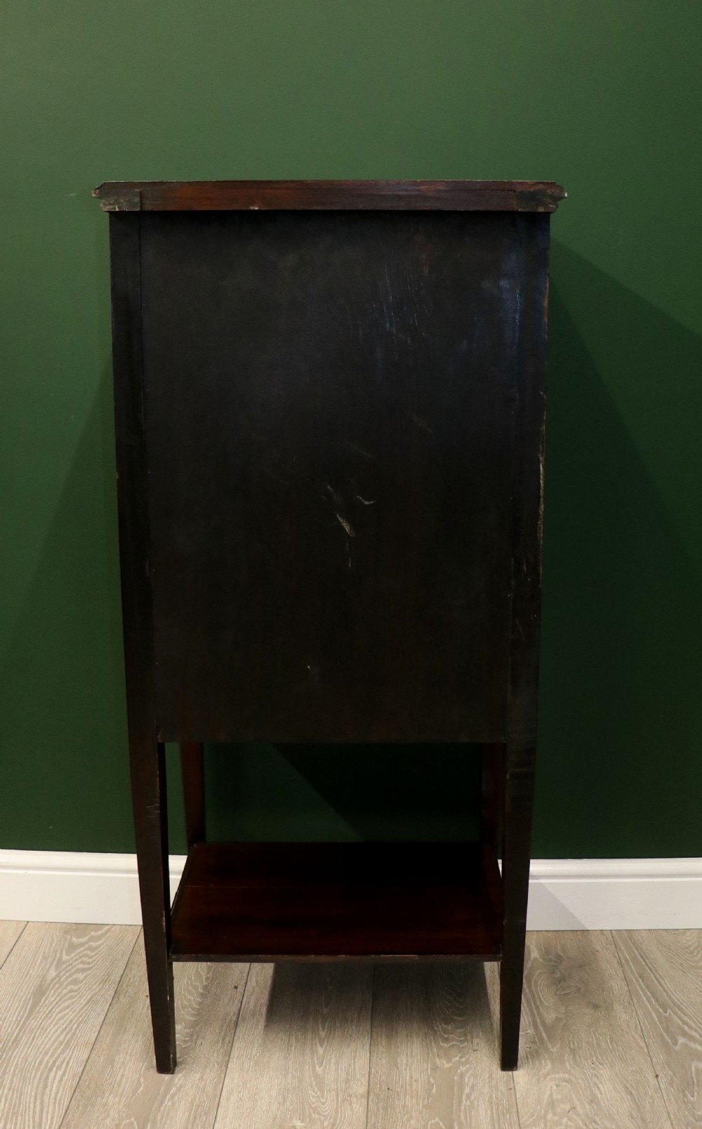 A tall, narrow dark mahogany music cabinet featuring seven fall-front drawers with central brass ring handles and an open shelf near the base. View X