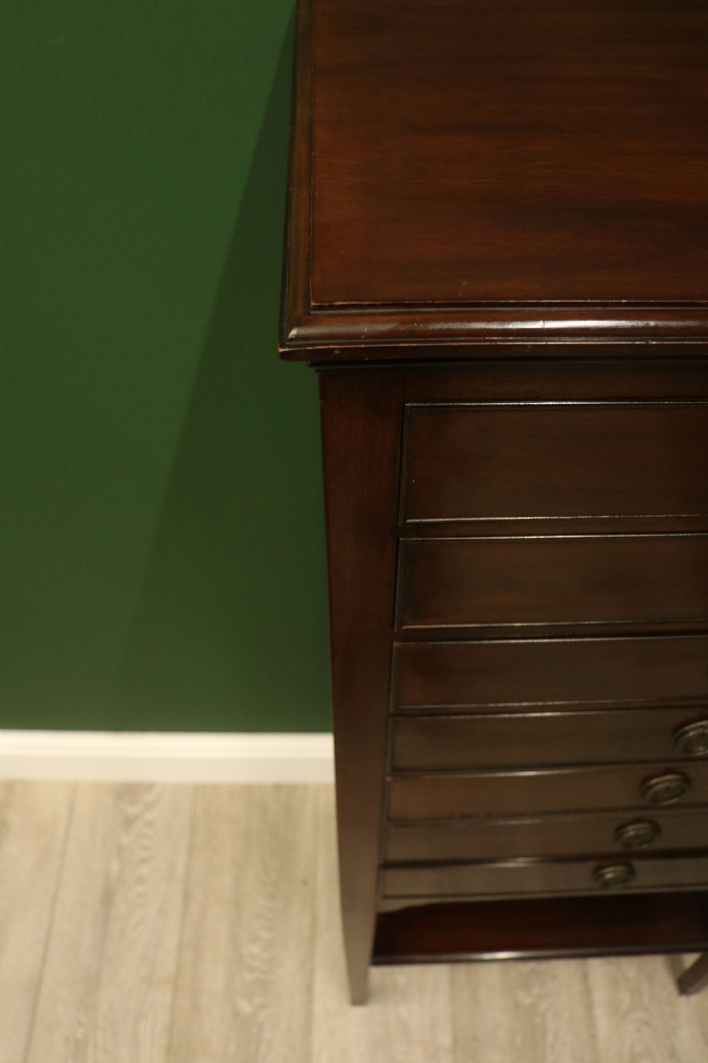 A tall, narrow dark mahogany music cabinet featuring seven fall-front drawers with central brass ring handles and an open shelf near the base. View XVI