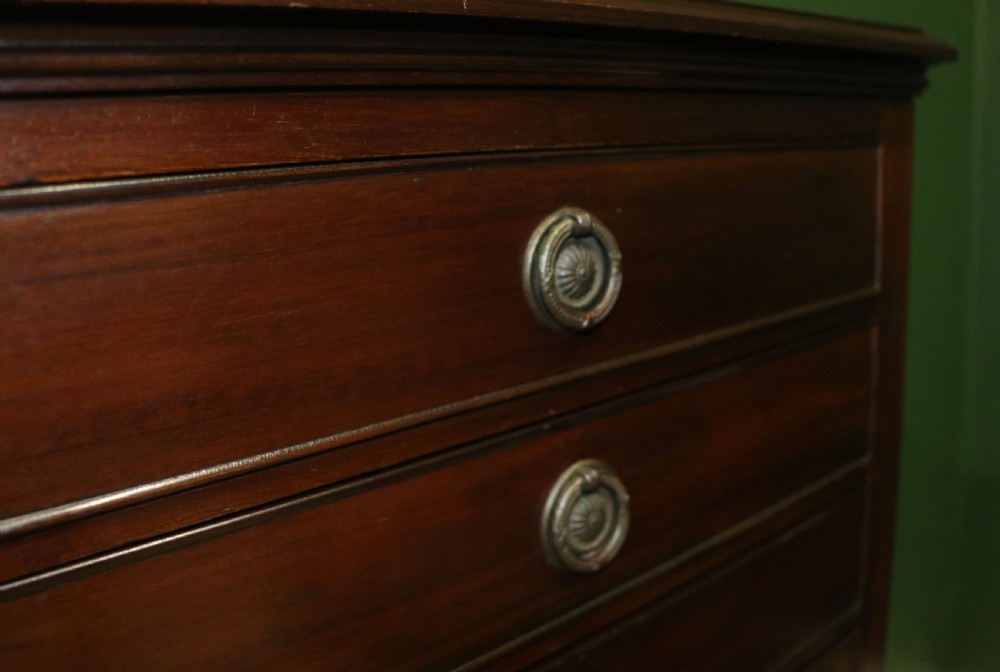 A tall, narrow dark mahogany music cabinet featuring seven fall-front drawers with central brass ring handles and an open shelf near the base. View XXI