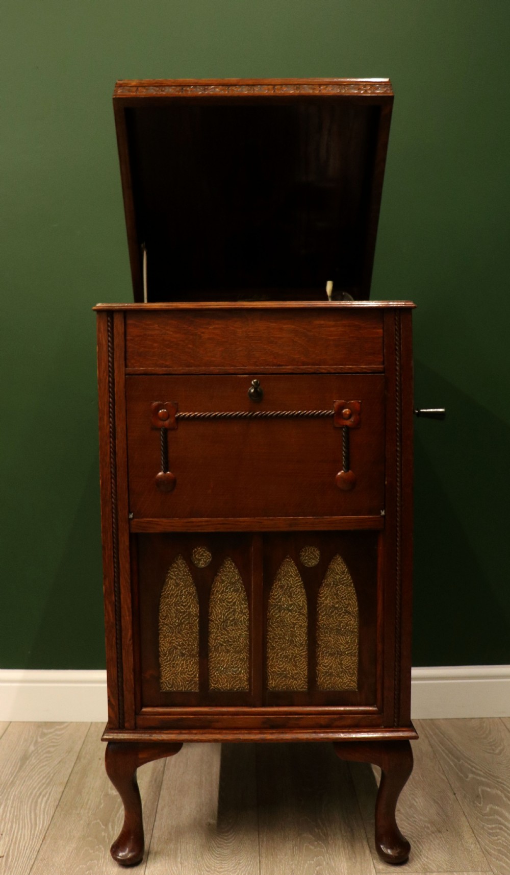 An upright dark oak parlour gramophone cabinet featuring cabriole legs, a hinged lid, carved rope detailing, and gothic arch fretwork grilles.