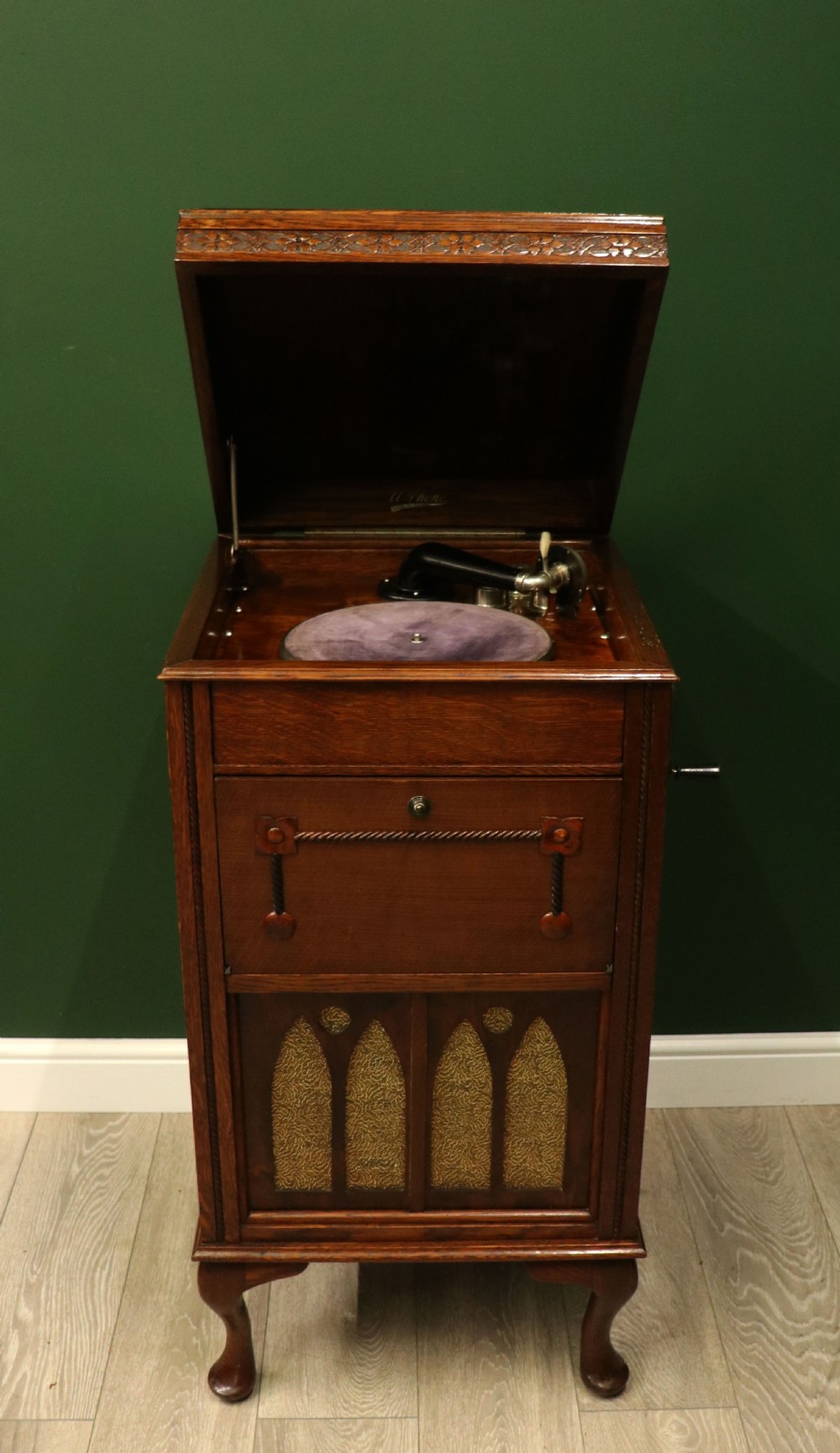 An upright dark oak parlour gramophone cabinet featuring cabriole legs, a hinged lid, carved rope detailing, and gothic arch fretwork grilles. View II