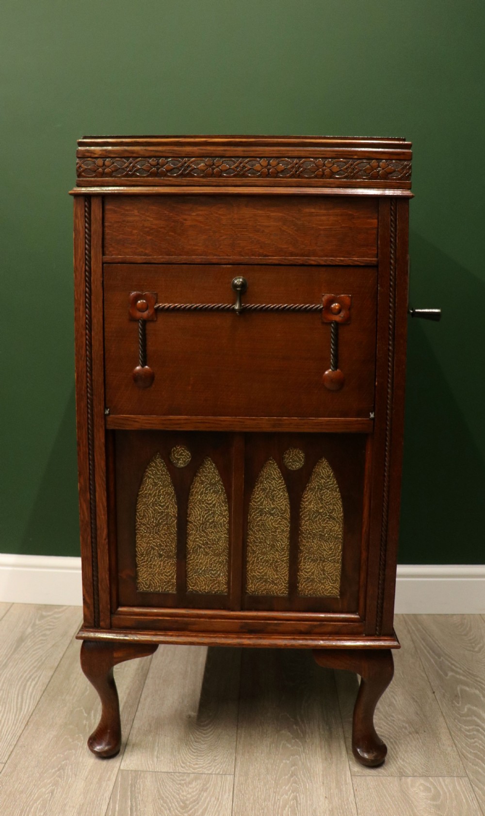 An upright dark oak parlour gramophone cabinet featuring cabriole legs, a hinged lid, carved rope detailing, and gothic arch fretwork grilles. View IV