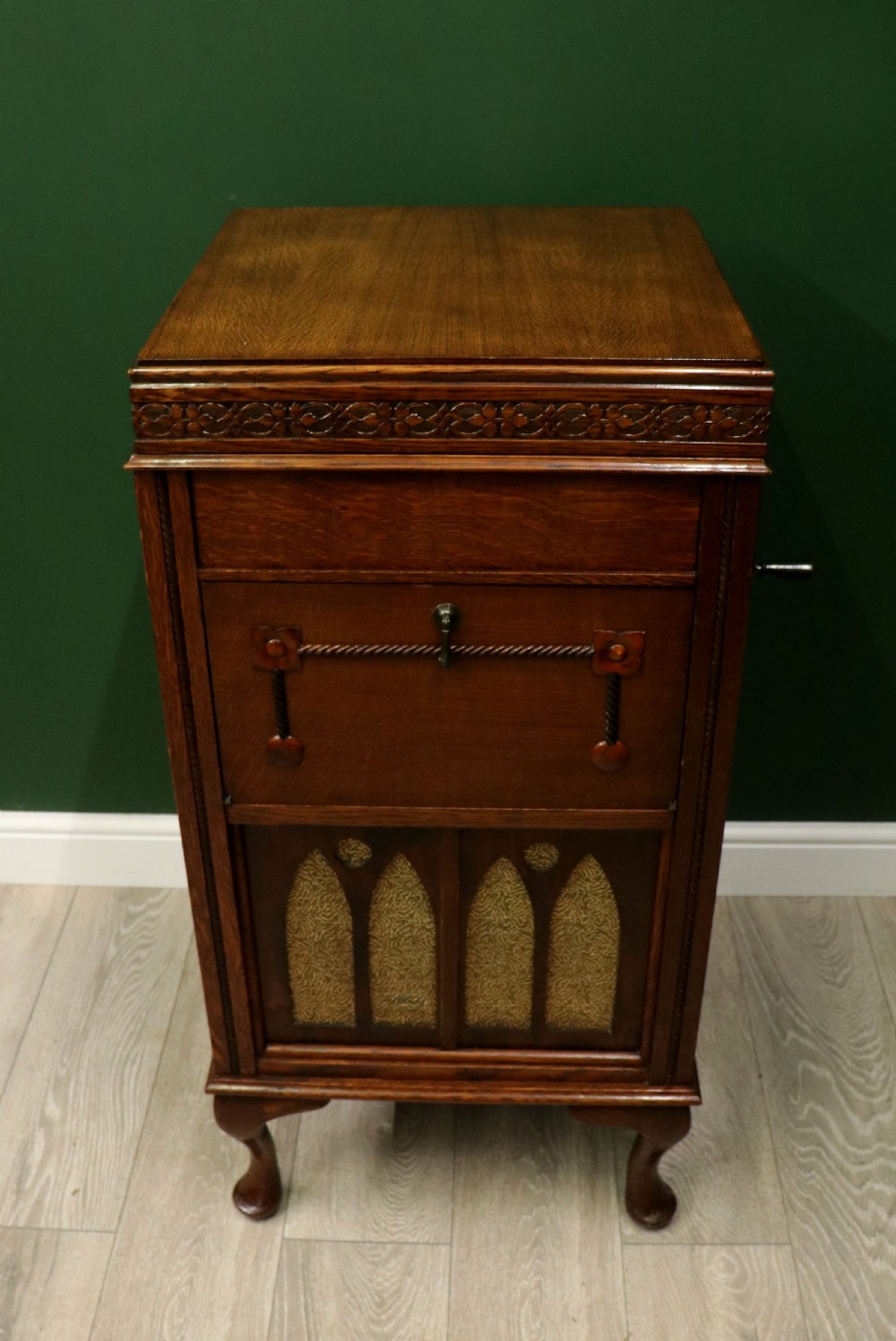 An upright dark oak parlour gramophone cabinet featuring cabriole legs, a hinged lid, carved rope detailing, and gothic arch fretwork grilles. View V