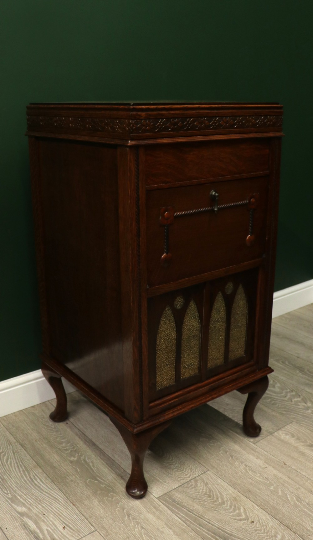 An upright dark oak parlour gramophone cabinet featuring cabriole legs, a hinged lid, carved rope detailing, and gothic arch fretwork grilles. View VI