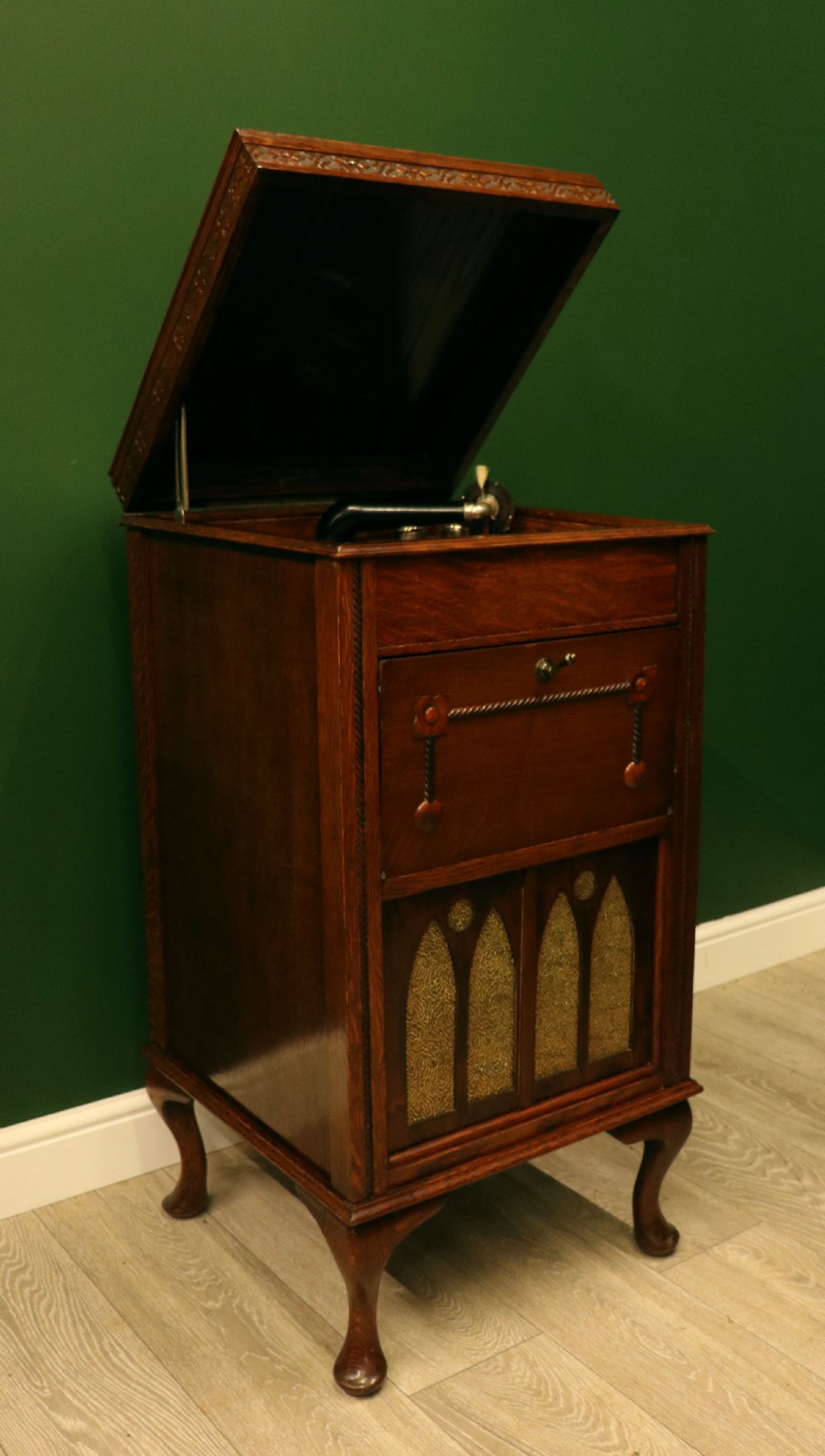 An upright dark oak parlour gramophone cabinet featuring cabriole legs, a hinged lid, carved rope detailing, and gothic arch fretwork grilles. View VII