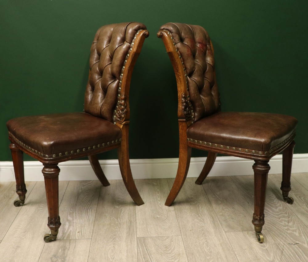 A pair of Victorian carved oak side chairs upholstered in deep-buttoned brown leather with brass studding and turned front legs on castors. View III