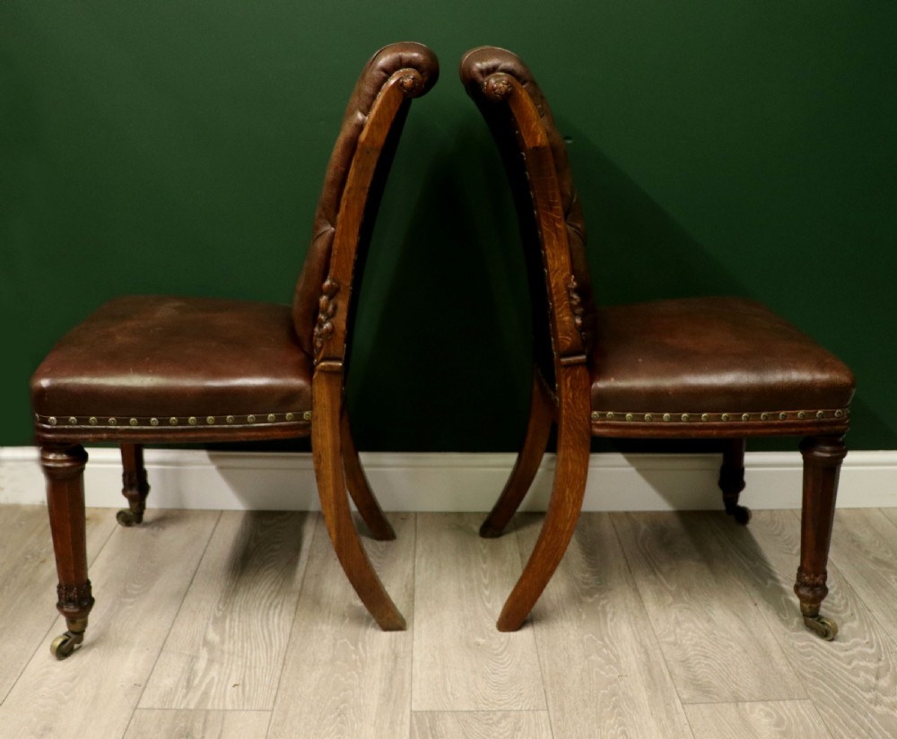 A pair of Victorian carved oak side chairs upholstered in deep-buttoned brown leather with brass studding and turned front legs on castors. View IV