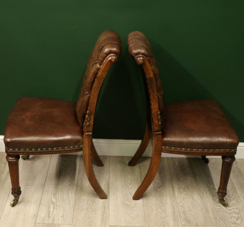 A pair of Victorian carved oak side chairs upholstered in deep-buttoned brown leather with brass studding and turned front legs on castors. View V