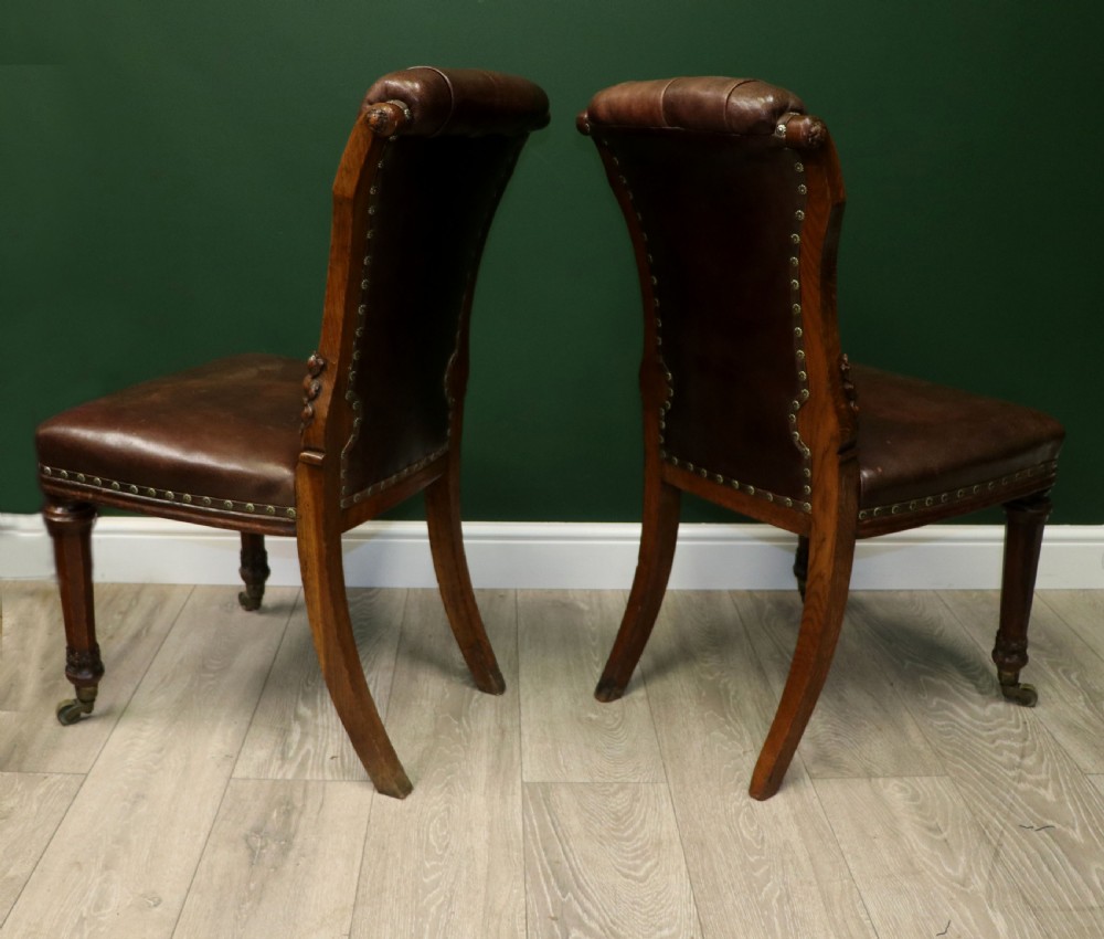 A pair of Victorian carved oak side chairs upholstered in deep-buttoned brown leather with brass studding and turned front legs on castors. View VI