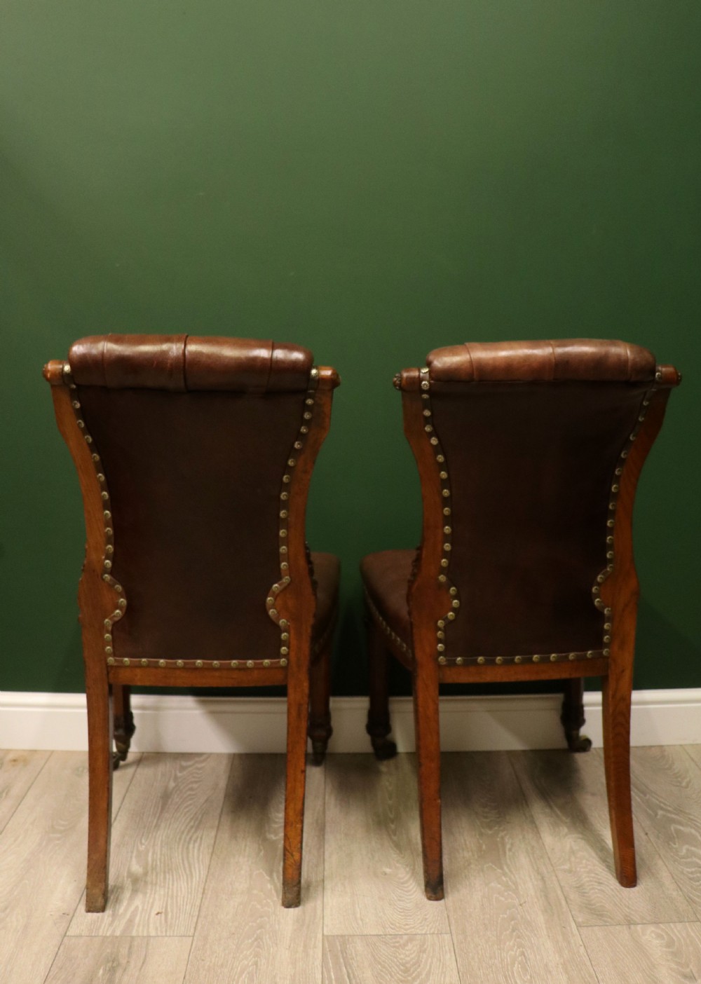 A pair of Victorian carved oak side chairs upholstered in deep-buttoned brown leather with brass studding and turned front legs on castors. View VII
