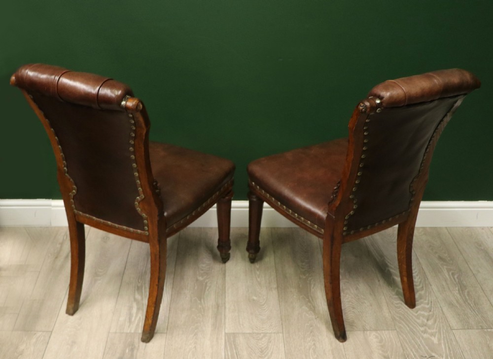 A pair of Victorian carved oak side chairs upholstered in deep-buttoned brown leather with brass studding and turned front legs on castors. View VIII