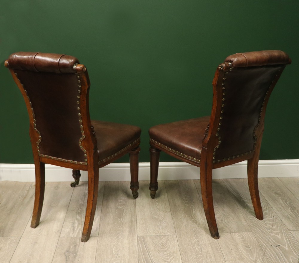 A pair of Victorian carved oak side chairs upholstered in deep-buttoned brown leather with brass studding and turned front legs on castors. View IX