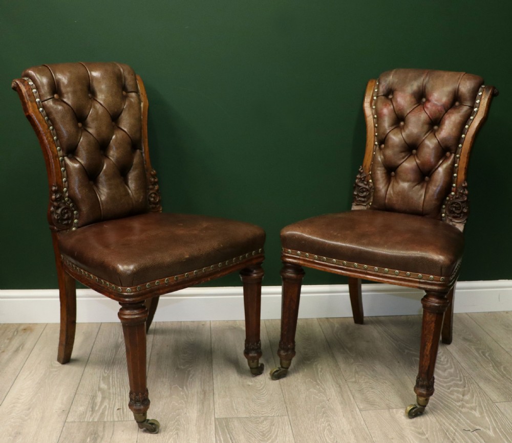 A pair of Victorian carved oak side chairs upholstered in deep-buttoned brown leather with brass studding and turned front legs on castors. View XI