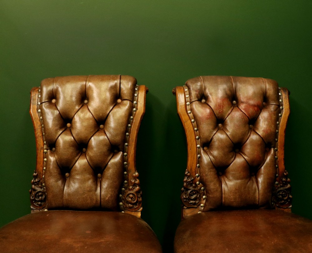 A pair of Victorian carved oak side chairs upholstered in deep-buttoned brown leather with brass studding and turned front legs on castors. View XII