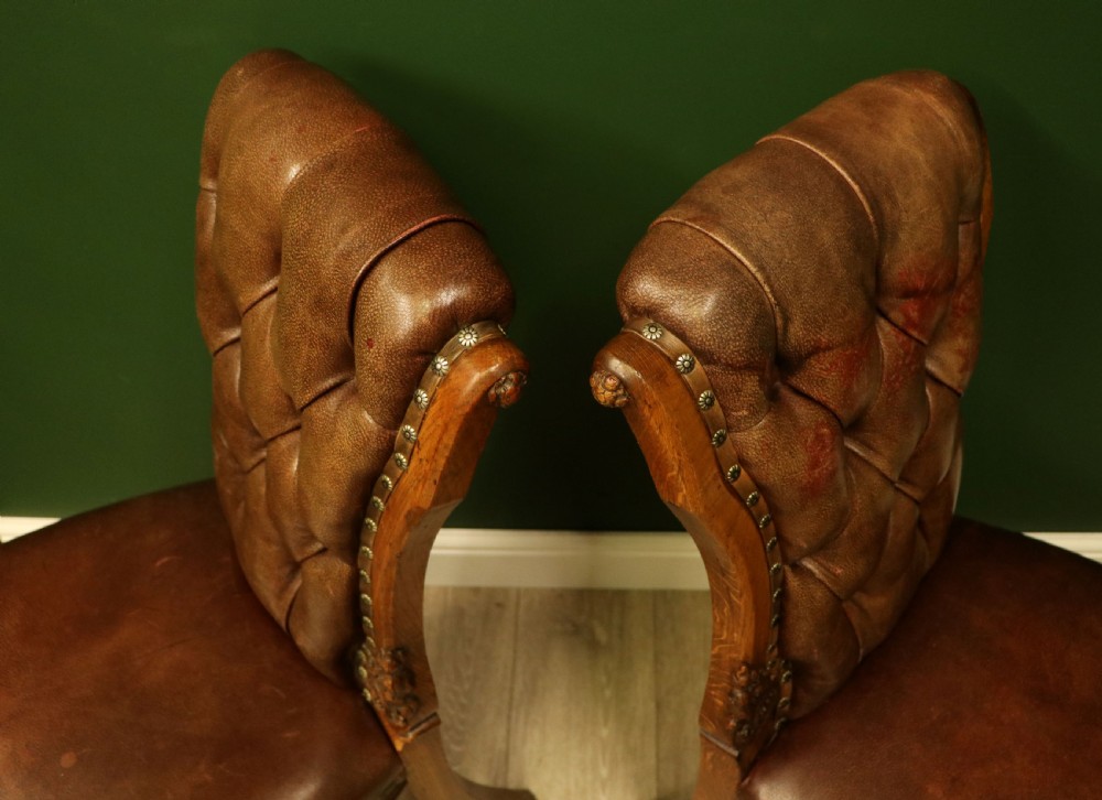 A pair of Victorian carved oak side chairs upholstered in deep-buttoned brown leather with brass studding and turned front legs on castors. View XIV