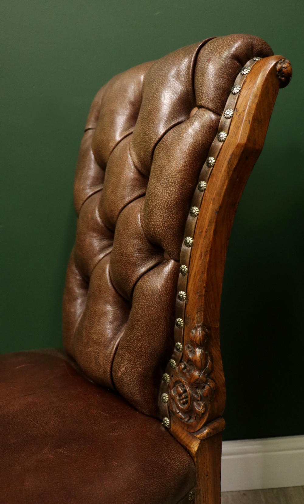 A pair of Victorian carved oak side chairs upholstered in deep-buttoned brown leather with brass studding and turned front legs on castors. View XV