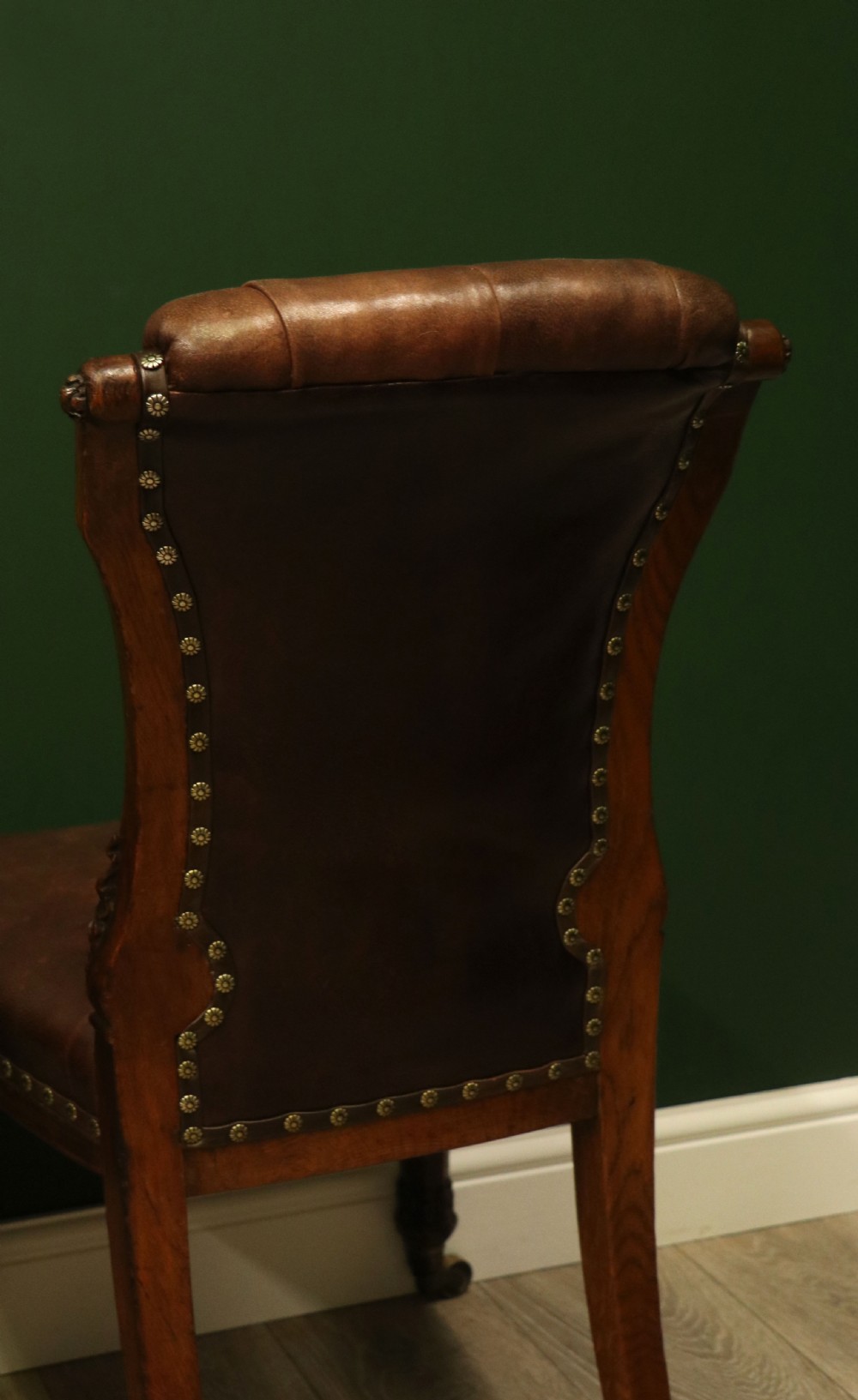A pair of Victorian carved oak side chairs upholstered in deep-buttoned brown leather with brass studding and turned front legs on castors. View XIX