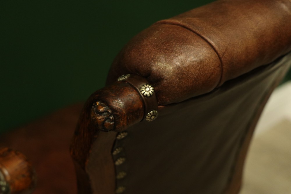 A pair of Victorian carved oak side chairs upholstered in deep-buttoned brown leather with brass studding and turned front legs on castors. View XXI