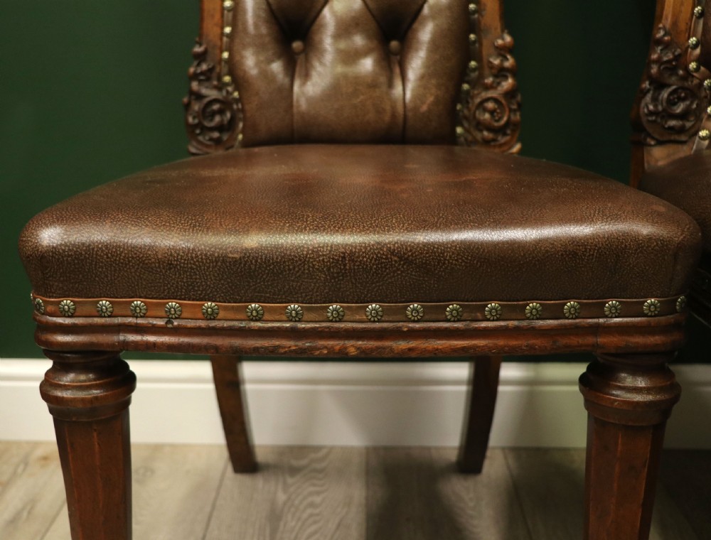 A pair of Victorian carved oak side chairs upholstered in deep-buttoned brown leather with brass studding and turned front legs on castors. View XXII