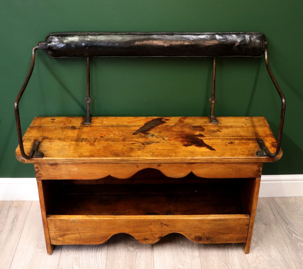 An antique pine wooden bench featuring a shaped aproned base, integrated lower shelf, wrought iron armrests, and a black leather padded cylindrical bolster backrest. View II