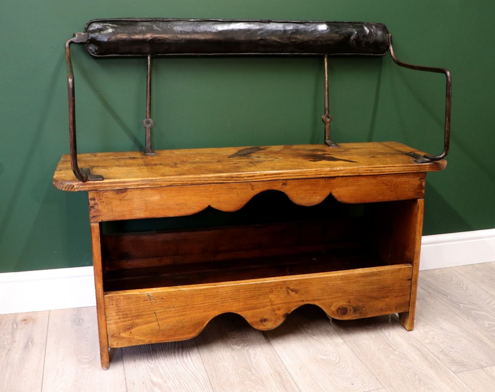 An antique pine wooden bench featuring a shaped aproned base, integrated lower shelf, wrought iron armrests, and a black leather padded cylindrical bolster backrest. View III