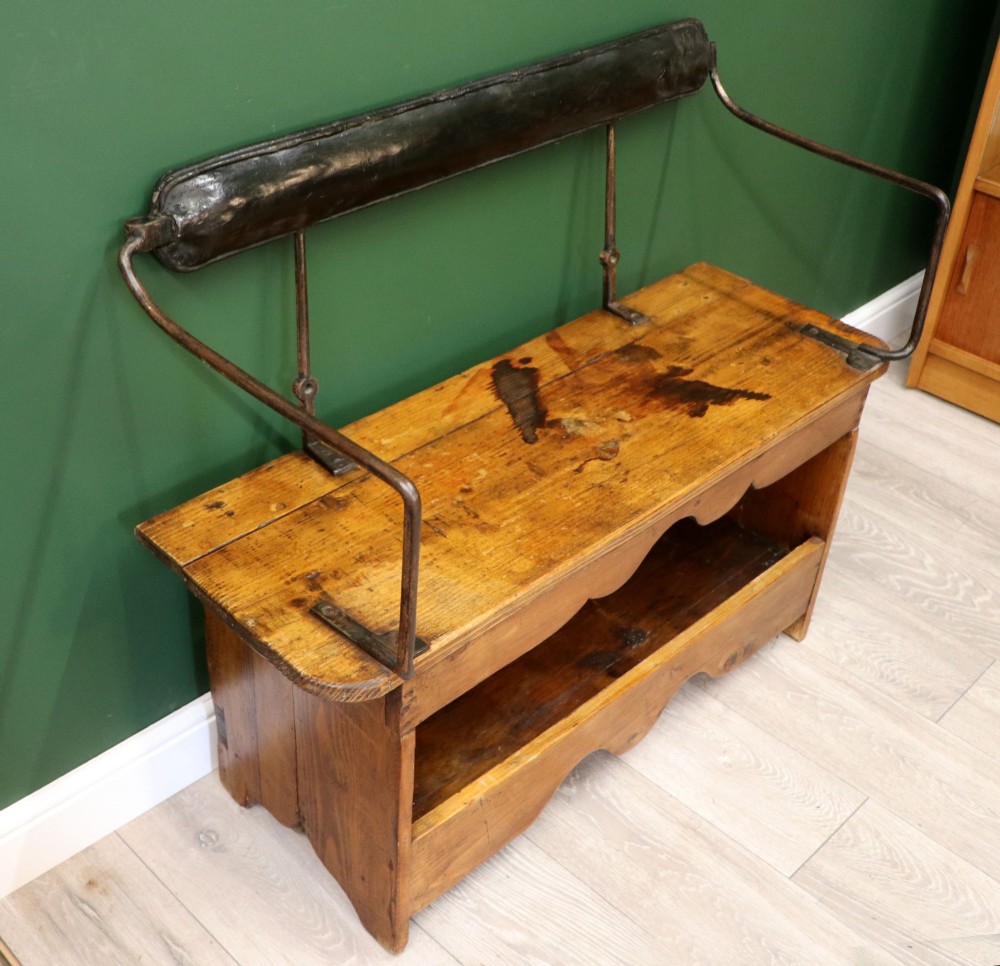 An antique pine wooden bench featuring a shaped aproned base, integrated lower shelf, wrought iron armrests, and a black leather padded cylindrical bolster backrest. View IV