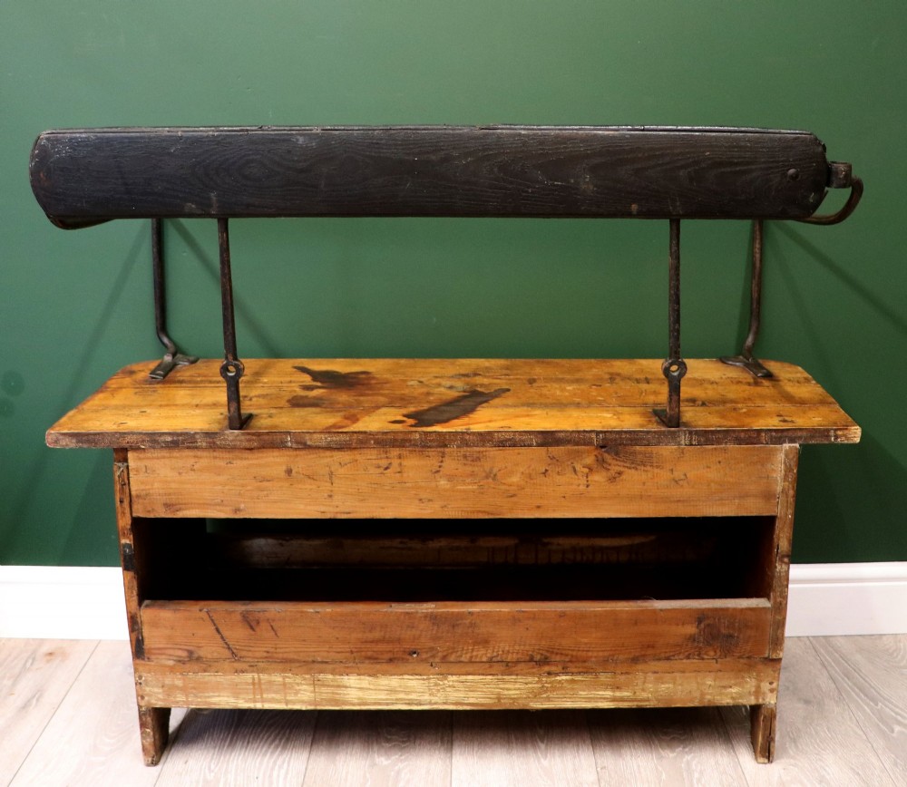 An antique pine wooden bench featuring a shaped aproned base, integrated lower shelf, wrought iron armrests, and a black leather padded cylindrical bolster backrest. View V