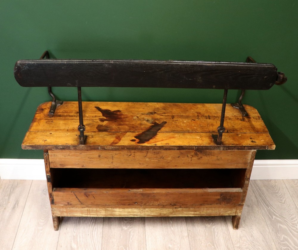 An antique pine wooden bench featuring a shaped aproned base, integrated lower shelf, wrought iron armrests, and a black leather padded cylindrical bolster backrest. View VI