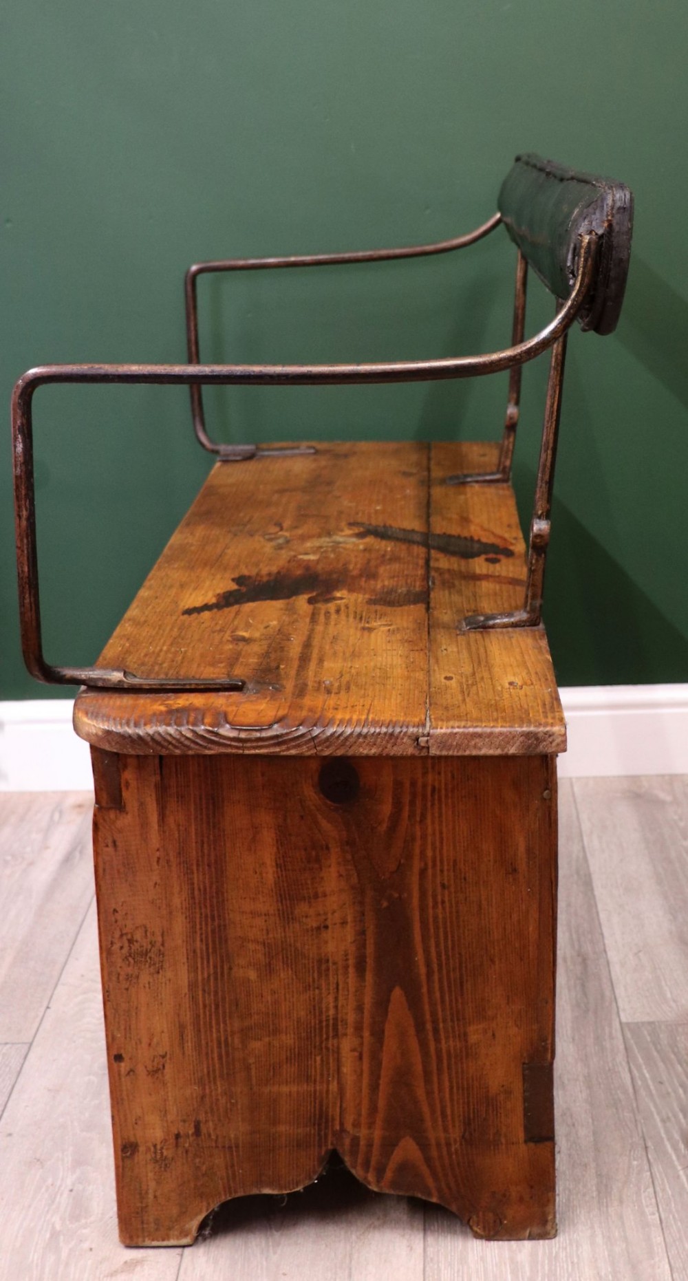 An antique pine wooden bench featuring a shaped aproned base, integrated lower shelf, wrought iron armrests, and a black leather padded cylindrical bolster backrest. View VII