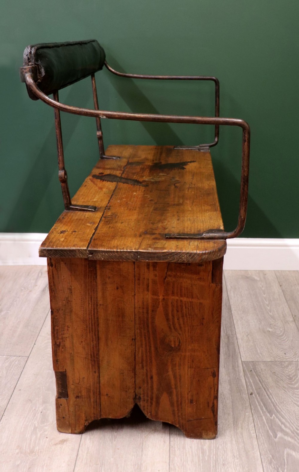 An antique pine wooden bench featuring a shaped aproned base, integrated lower shelf, wrought iron armrests, and a black leather padded cylindrical bolster backrest. View IX