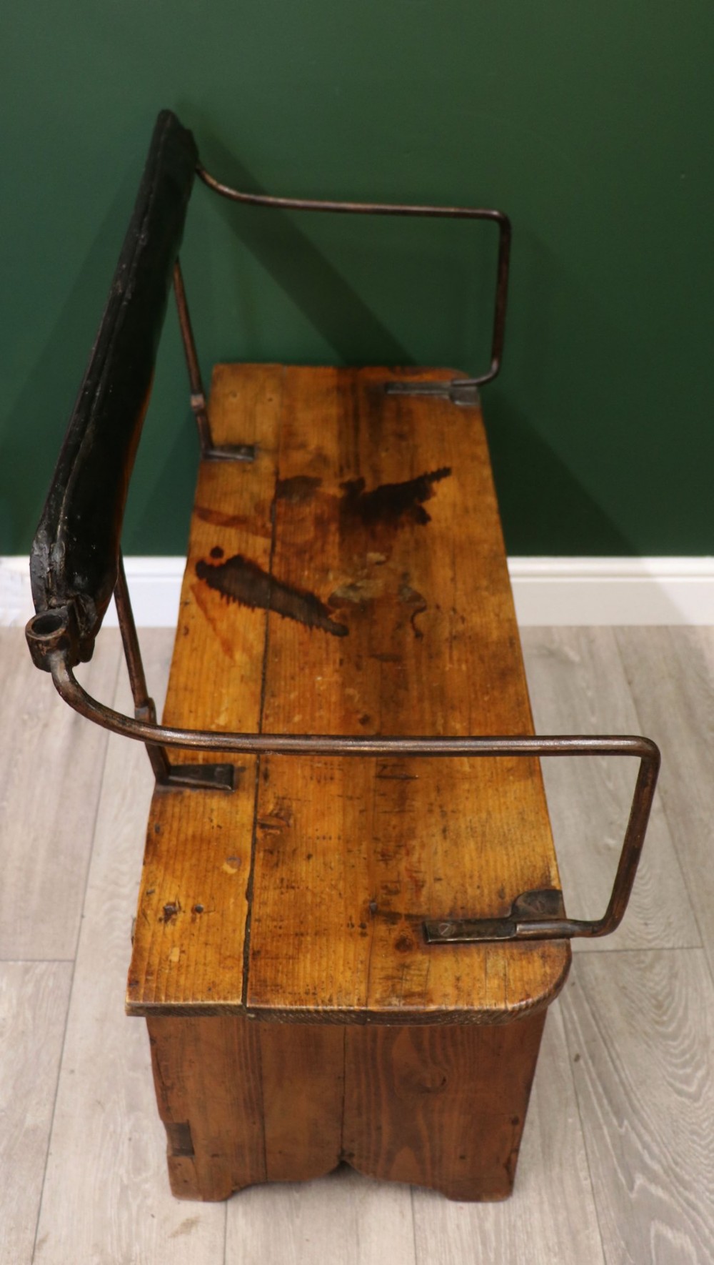 An antique pine wooden bench featuring a shaped aproned base, integrated lower shelf, wrought iron armrests, and a black leather padded cylindrical bolster backrest. View X