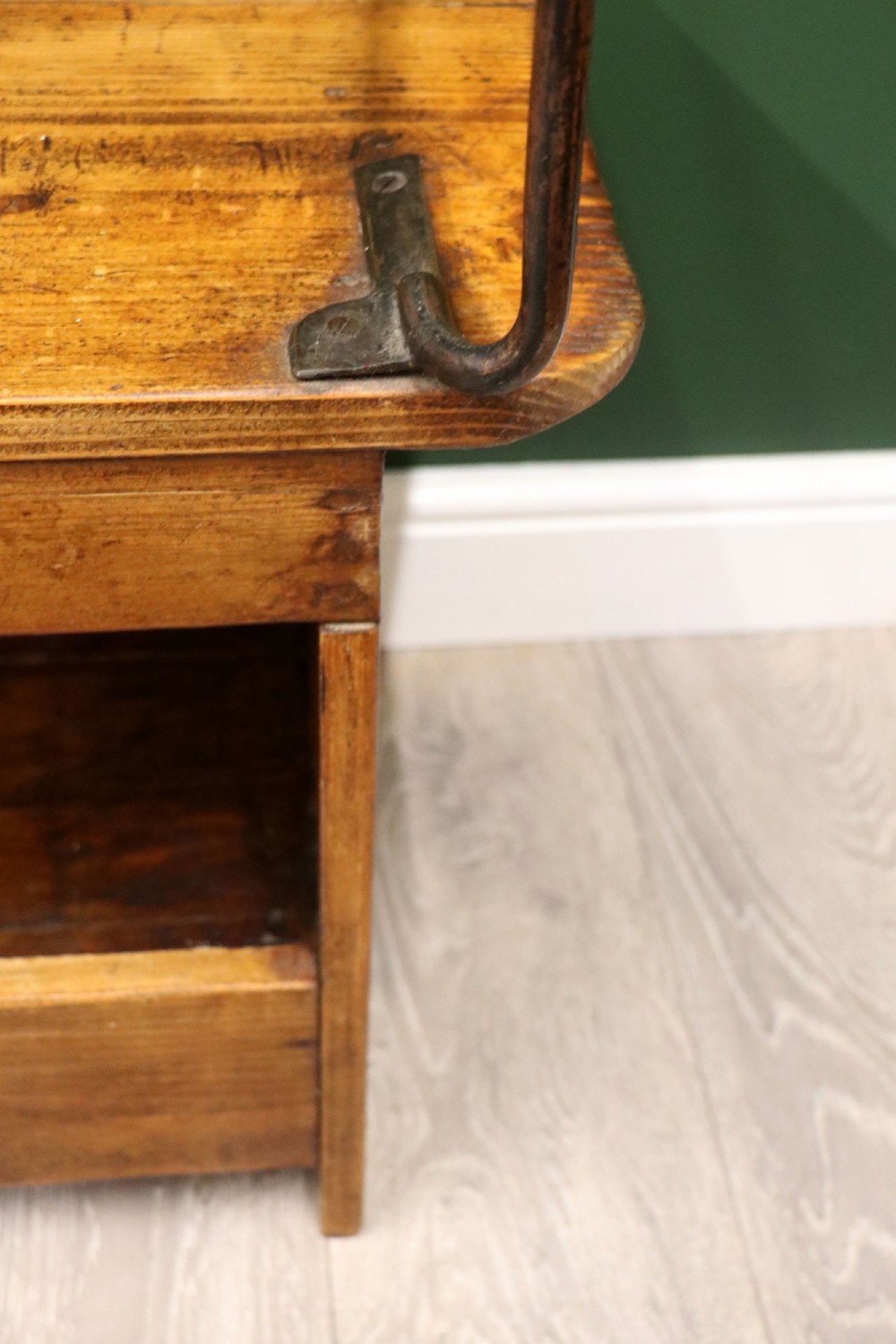 An antique pine wooden bench featuring a shaped aproned base, integrated lower shelf, wrought iron armrests, and a black leather padded cylindrical bolster backrest. View XIV