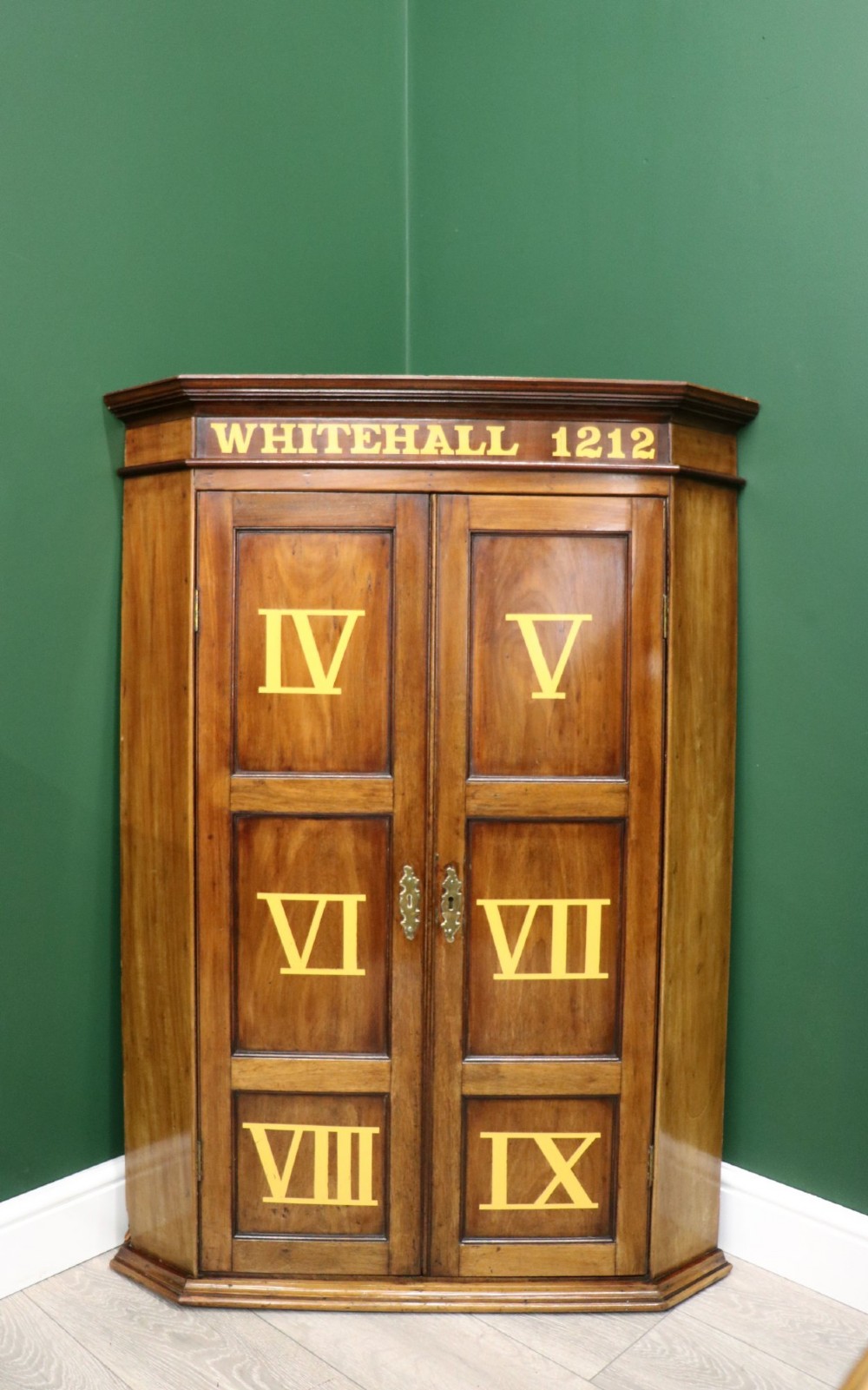 A George III mahogany wall-mounted corner cabinet with double panelled doors featuring painted yellow Roman numerals and a top frieze reading WHITEHALL 1212.