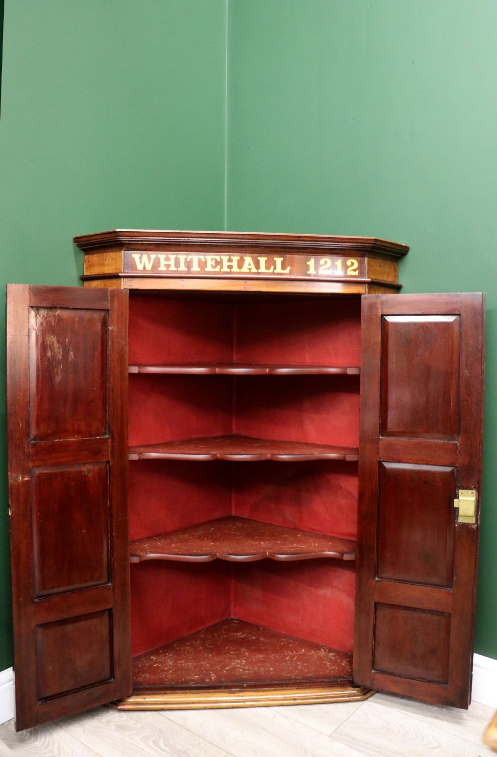 A George III mahogany wall-mounted corner cabinet with double panelled doors featuring painted yellow Roman numerals and a top frieze reading WHITEHALL 1212. View III