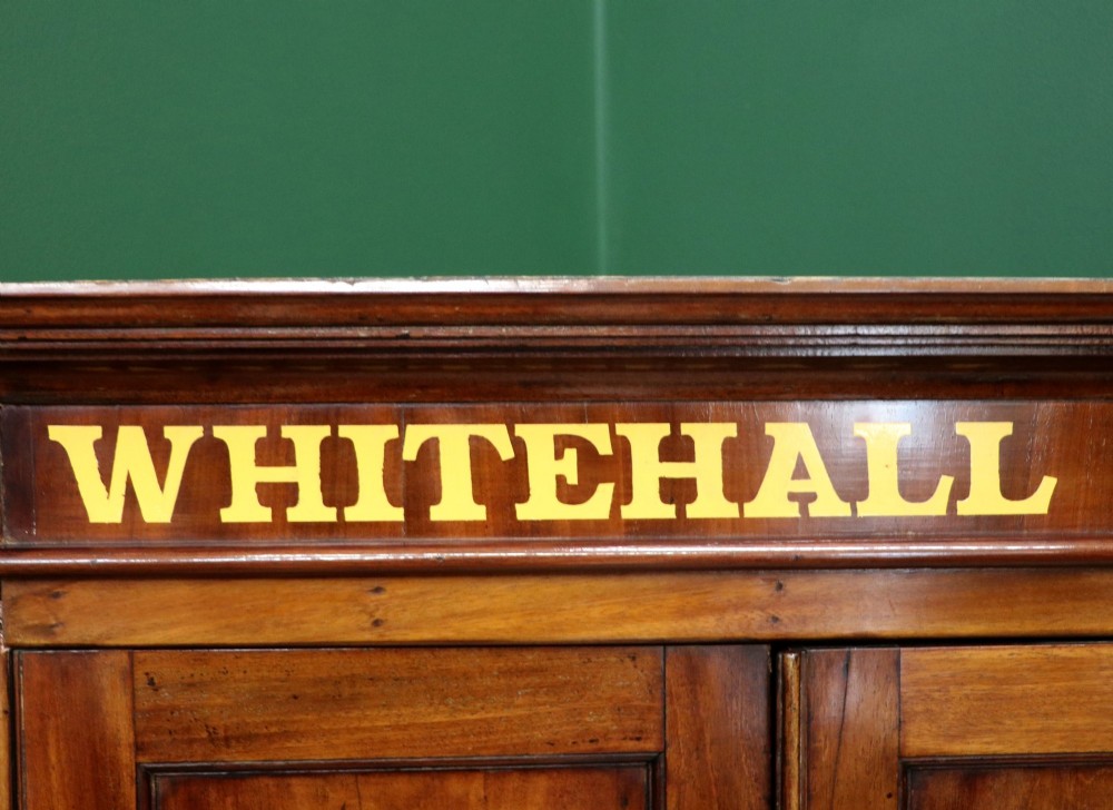 A George III mahogany wall-mounted corner cabinet with double panelled doors featuring painted yellow Roman numerals and a top frieze reading WHITEHALL 1212. View VI