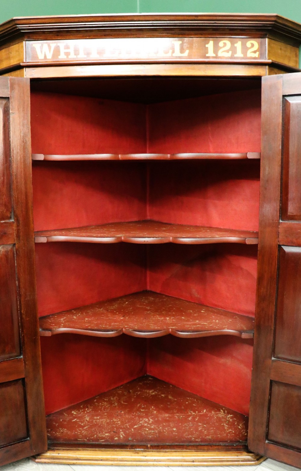 A George III mahogany wall-mounted corner cabinet with double panelled doors featuring painted yellow Roman numerals and a top frieze reading WHITEHALL 1212. View XII