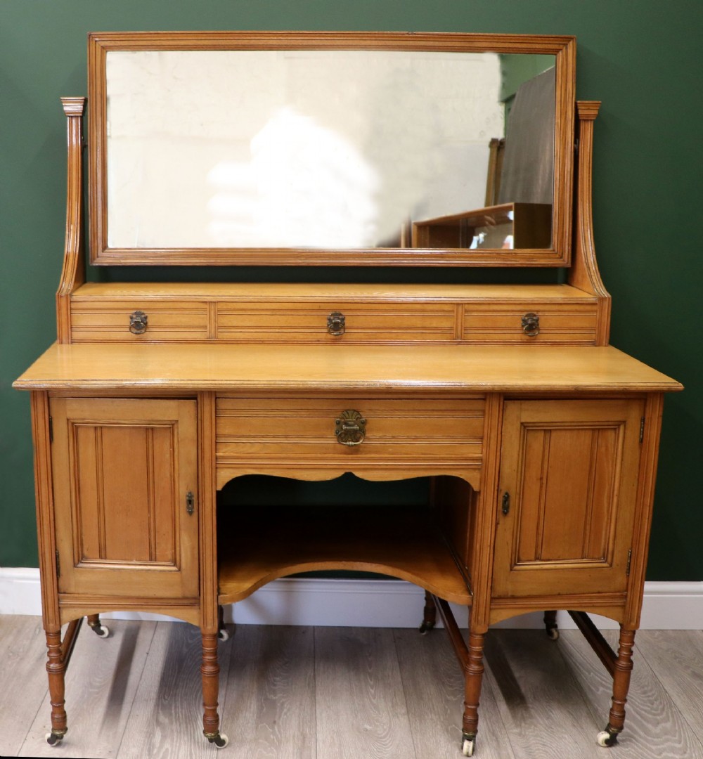 A late Victorian light walnut dressing table featuring an attached rectangular mirror, three small upper drawers, two panelled side cupboards, and turned legs with castors.