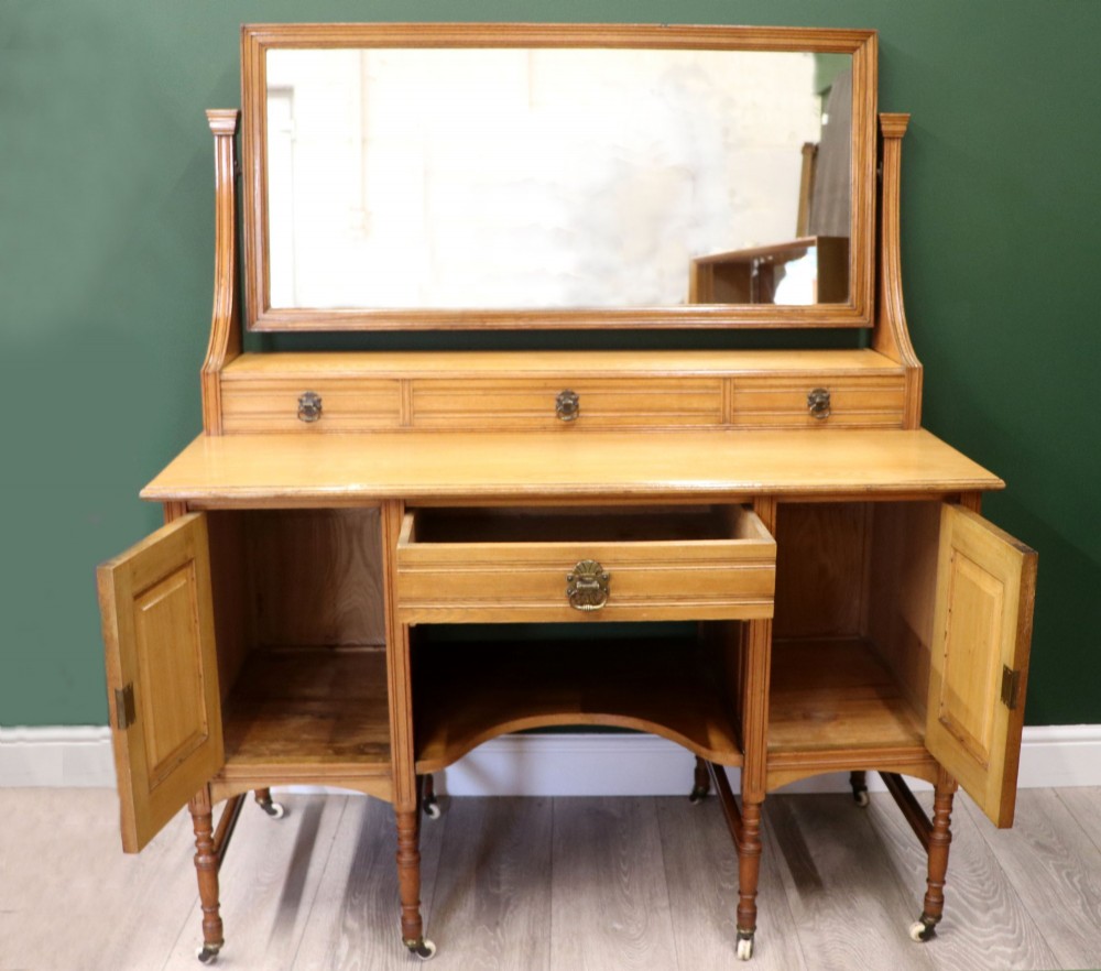 A late Victorian light walnut dressing table featuring an attached rectangular mirror, three small upper drawers, two panelled side cupboards, and turned legs with castors. View II