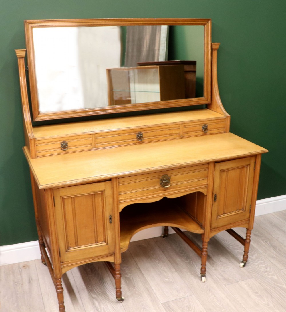 A late Victorian light walnut dressing table featuring an attached rectangular mirror, three small upper drawers, two panelled side cupboards, and turned legs with castors. View III