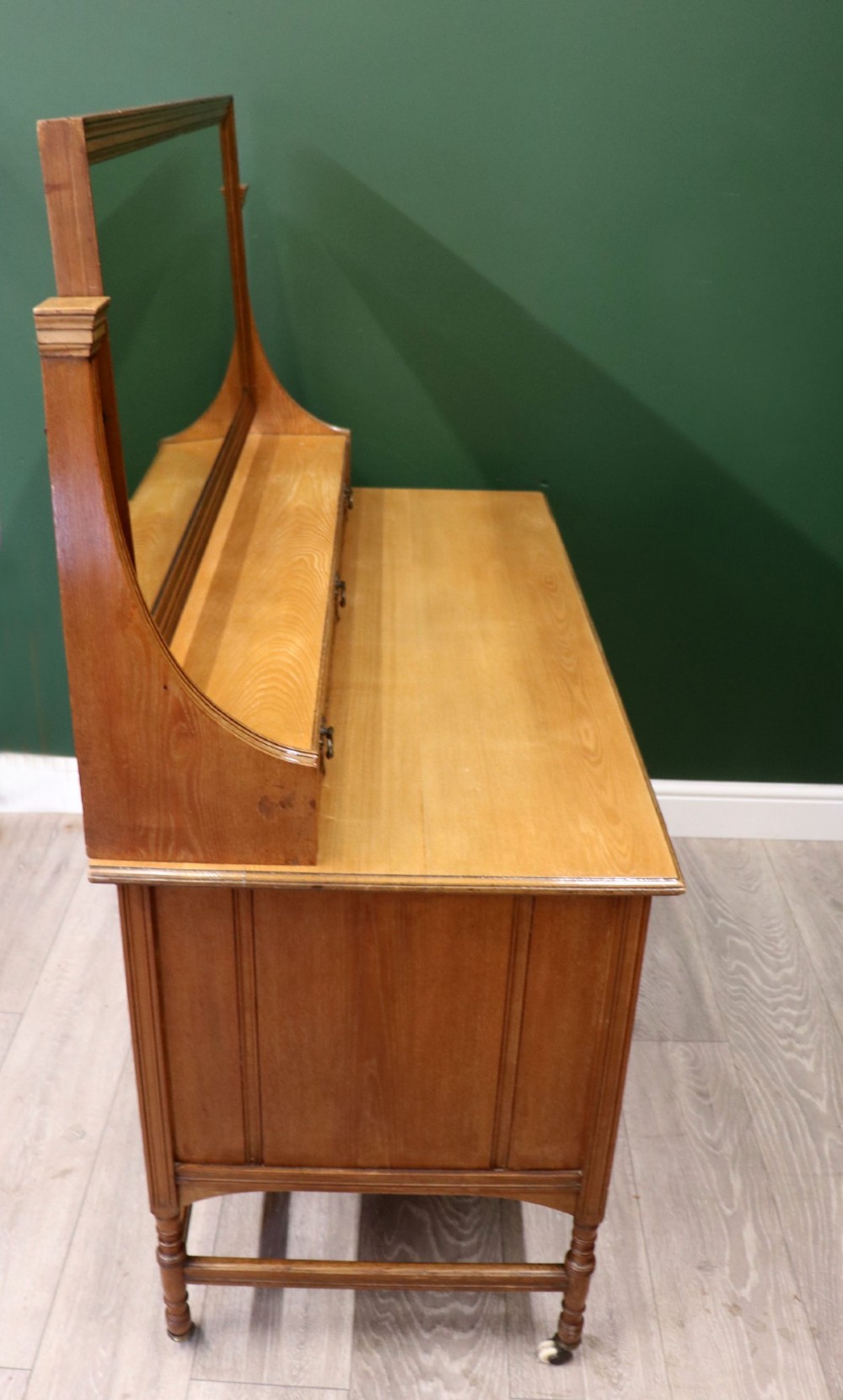 A late Victorian light walnut dressing table featuring an attached rectangular mirror, three small upper drawers, two panelled side cupboards, and turned legs with castors. View IV